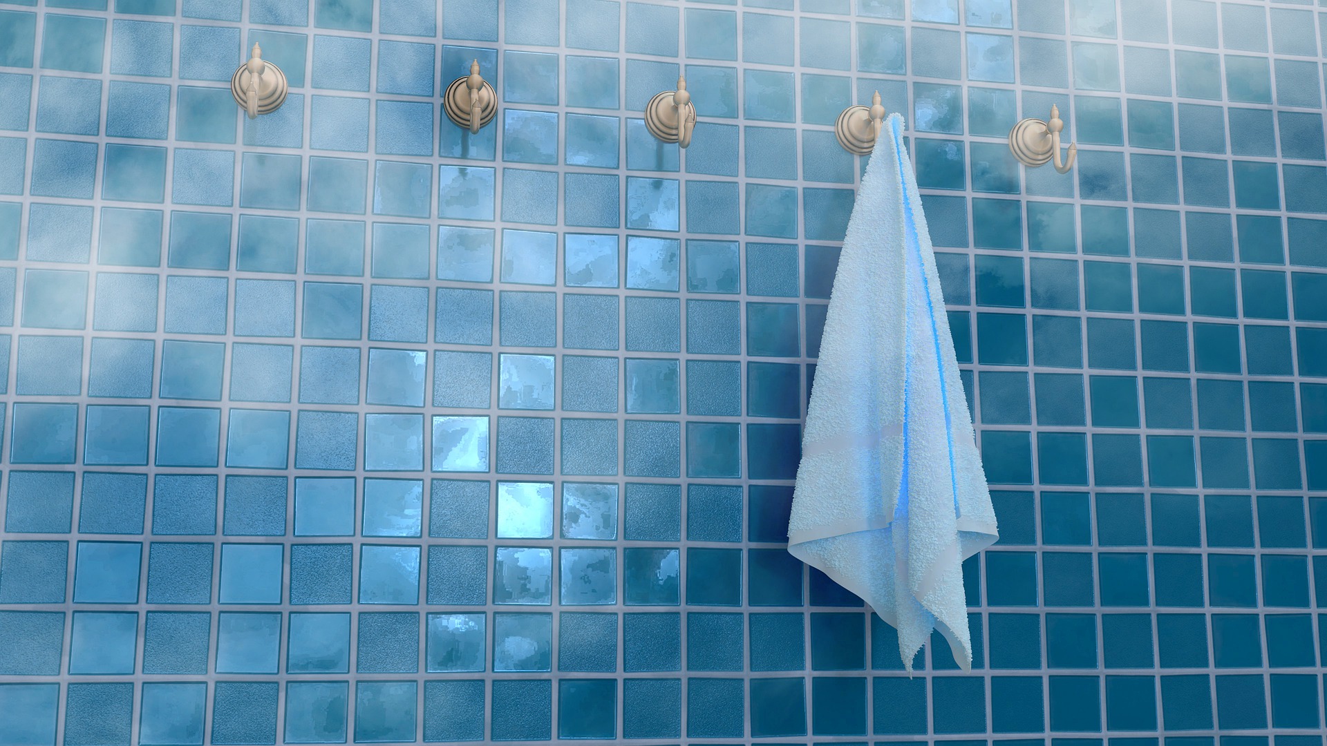 Badezimmer mit blauen Kacheln und mit Handtuchhaltern an der Wand, an denen ein weisses Handtuch hängt.